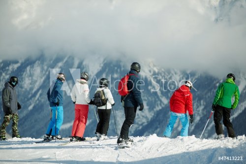 Group of young skiers stands on edge of snowy hillslope