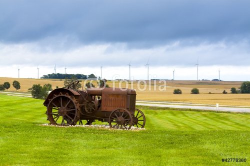 Old rusty tractor with wind turbines in the background. - 900458219