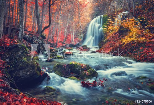 Autumn forest with waterfall at mountain river at sunset.