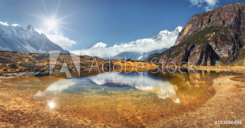 Beautiful scene with high rocks with snow covered peaks, mountain lake, reflection in water, blue sky with clouds in sunset. Nepal.