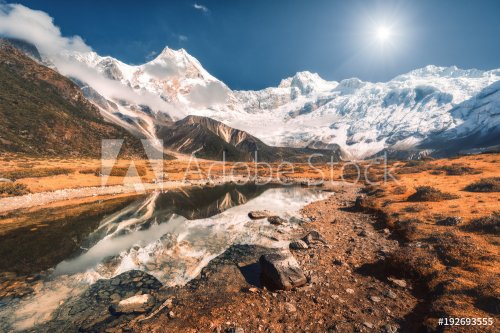 Beautiful scene with high rocks with snow covered peaks, stones in mountain lake, reflection in water, blue sky in sunset. Nepal.