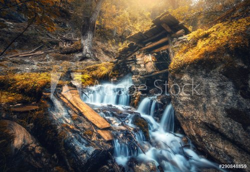 Stony well in colorful forest with little waterfall in mountain river at sunset in autumn.