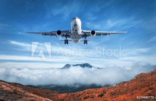 Airplane is flying over low clouds and mountains with autumn forest