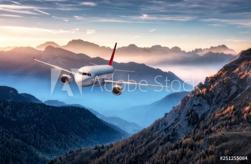 Airplane is flying over mountains in fog at colorful sunset in summer.