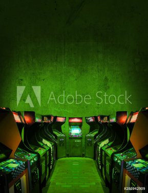 Old Unbranded Vintage Arcade Video Games in a dark gaming room with green light with glowing displays and concrete wall