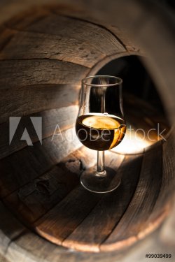 A glass of whiskey on a background of oak barrels - 901147356