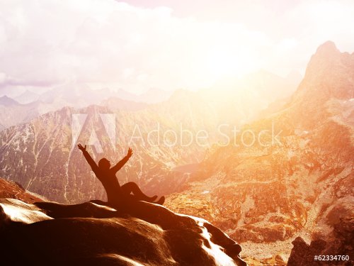 A happy man sitting on the peak of a mountain with hands raised - 901148962
