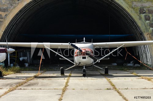 A small two-seater aircraft is in a hangar at the airport. pinned to the ground