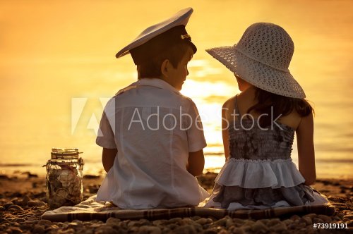 Boy and girl sitting on the shore of the lake at sunset - 901144118