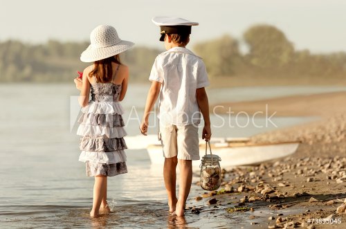 Boy with girl walking along the shore of the lake - 901144117