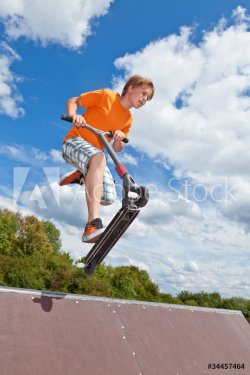 boyx jumping with his scooter at the skate park - 900379854