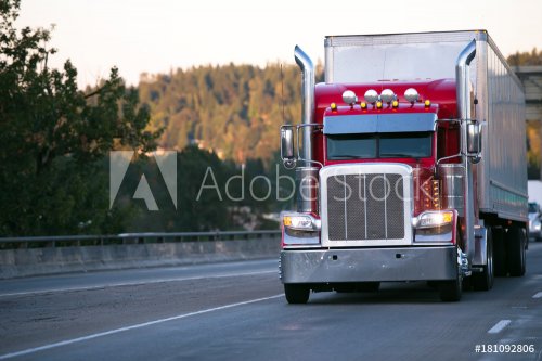 Bright red classic big rig semi truck with trailer move on evening road with turn on headlight