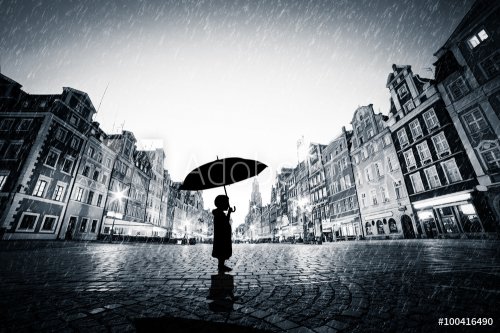 Child with umbrella standing alone on cobblestone old town in rain