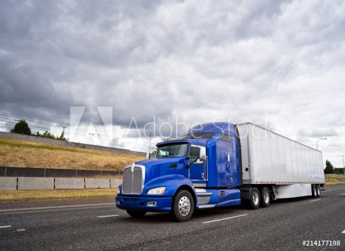 Classic blue big rig semi truck with dry van semi trailer going on wide highw... - 901154283