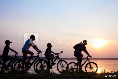 family on bicycles admiring the sunset on the lake. silhouette - 900458271