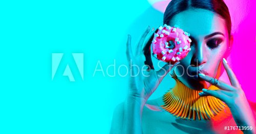 Fashion model woman posing in studio with donut in colorful bright lights