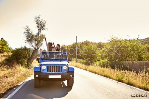 Four friends on the road in open car, two women standing - 901153185