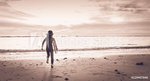 girl dressed in a wetsuit runs on the beach - 901148773