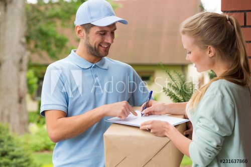 Happy courier in blue uniform and woman signing receipt of package delivery