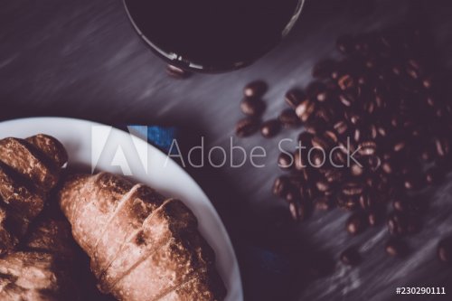 Macro shot of fresh croissants and coffee on a black background. Dessert and coffee beans. Mate moody color. concept of breakfast. Top view.