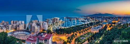 Night aerial panorama of Malaga, Spain with skyscrapers, streets, port, city hall and park during golden hour
