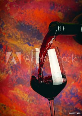 Red wine pouring in glass over grange background