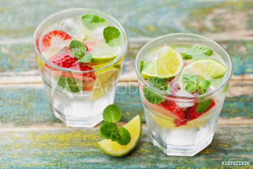 Summer lemonade or cocktail with lime, ice, strawberry and green mint in glass on rustic wooden table, mojito