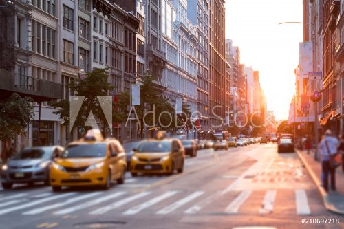 Sunlight shines down a busy street in New York City with taxis stopped at the intersection