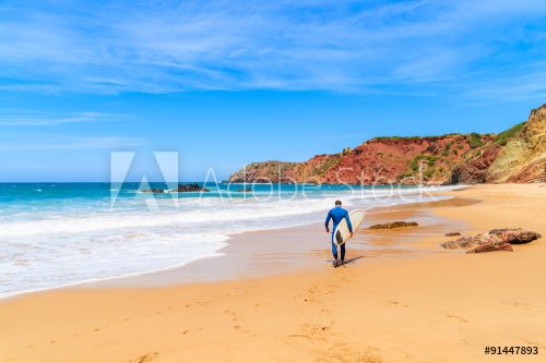 Surfer walking on Praia do Amado beach on sunny summer day, Algarve region, Portugal