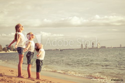 Three happy children standing on the beach - 901144128