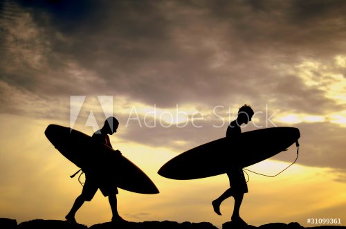 Two Surfers Carrying Their Boards Home At Sunset - 900296969