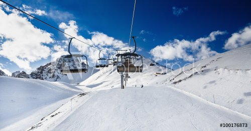 Winter mountains panorama with ski slopes and ski lifts. Skiers going down the slope under ski lift.