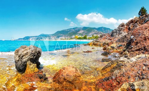 Amazing view on rocky tropical beach on sunny summer day in Alanya, Turkey. Turkish seascape with mountains and rocks on coastline. Blue clear sky, sea and tropic nature. Lagoon of mediterranean sea.