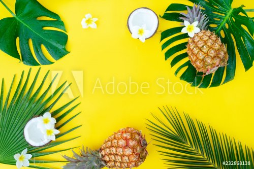 Summer flat lay frame with fresh tropical green leaves, coco and pineapples frame on yellow background