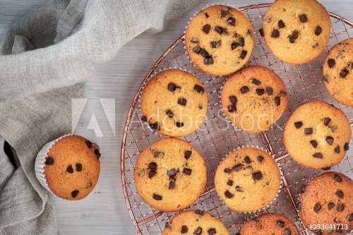 Twelve freshly baked choco chip muffins cooling off on wire mesh on wood with linen towel