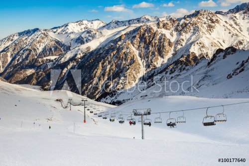 Winter mountains panorama with ski slopes and ski lifts. Skiers going down the slope under ski lift.