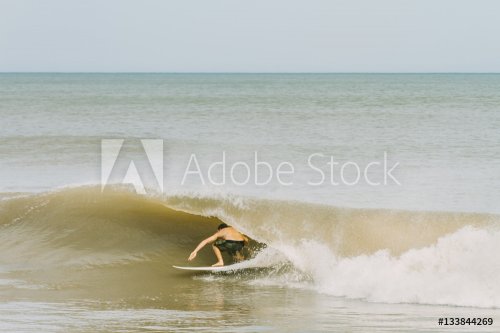 Young man tries to get under a wave while surfing on the shores