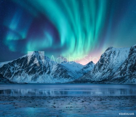 Aurora borealis over the snowy mountains, coast of the lake and reflection in water. Northern lights above snow covered rocks. Winter landscape with polar lights, fjord.