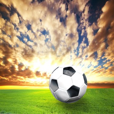 Football, soccer ball on green grass at sunset