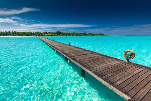 Long wooden jetty over atoll and a tropical island in Maldives - 901147395