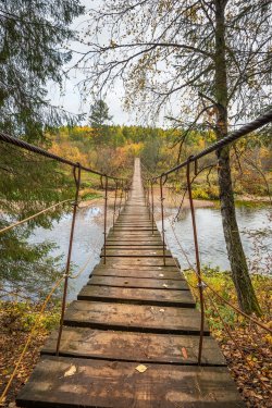 Wooden suspension bridge over the river in the forest - 901147959