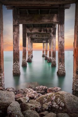 Underneath the pylons of a long jetty pier beach overlooking the
