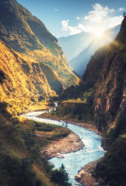Colorful landscape with high Himalayan mountains, beautiful curving river, green forest, blue sky with clouds and yellow sunlight at sunset in autumn in Nepal.
