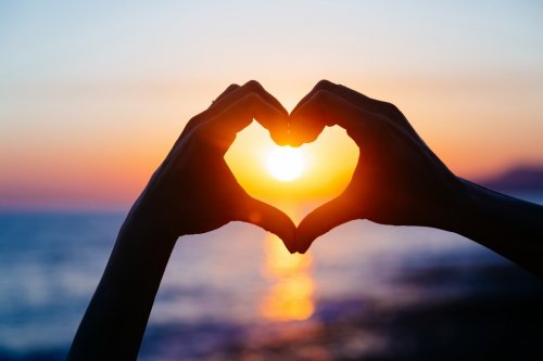 hands forming a heart shape with sunset silhouette - 901155410