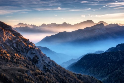 Mountains in fog at beautiful sunset in autumn in Dolomites, Italy. Landscape with alpine mountain valley, low clouds, trees on hills.