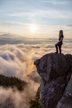 Adventurous Female Hiker on top of a mountain covered in clouds during a vibrant summer sunset. Taken on top of St Mark's Summit, West Vancouver, British Columbia