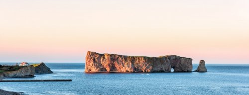 Famous large Rocher Perce rock in Gaspe Peninsula, Quebec, Gaspesie region, Canada at sunset, Saint Lawrence gulf, boat, ship, houses, wharf, dock, pier