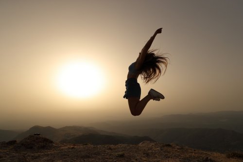 Silhouette de femme sautant au coucher du soleil sur la montagne - 901157450