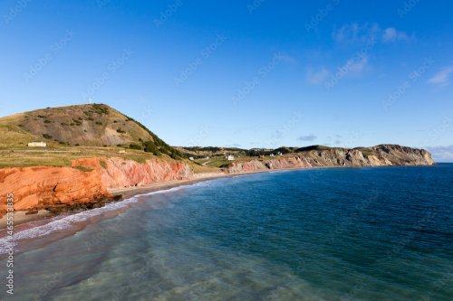 High angle view of the Petite Echouerie beach at the foot of red and grey sandstone cliffs, with houses in soft focus background, Havre-aux-Maisons, Magdalen Islands, Quebec, Canada