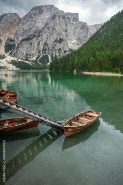 Barque et passerelle sur un lac vert avec des montagnes en arrière plan - 901157857